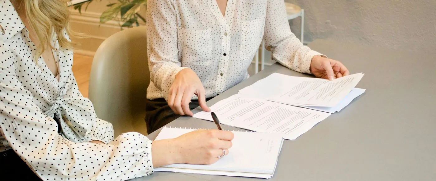 Two colleagues going through printed documents and taking notes at a table