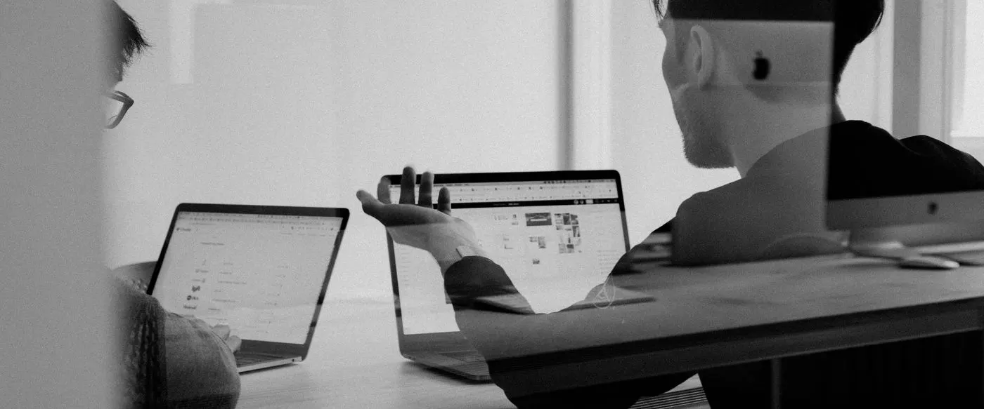 Two colleagues working at laptops, seen through a glass partition