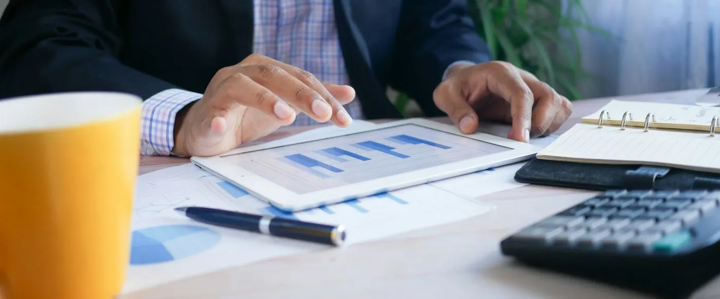 A person reviewing charts on a tablet beside printed reports and a calculator