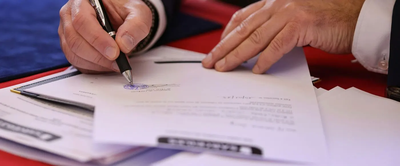 Hands signing and stamping a printed agreement at a desk