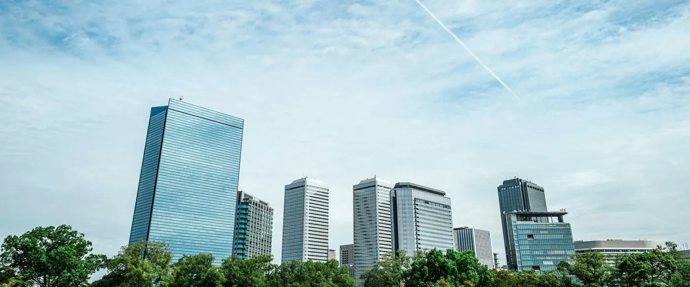 Office towers rising above trees under a wide sky