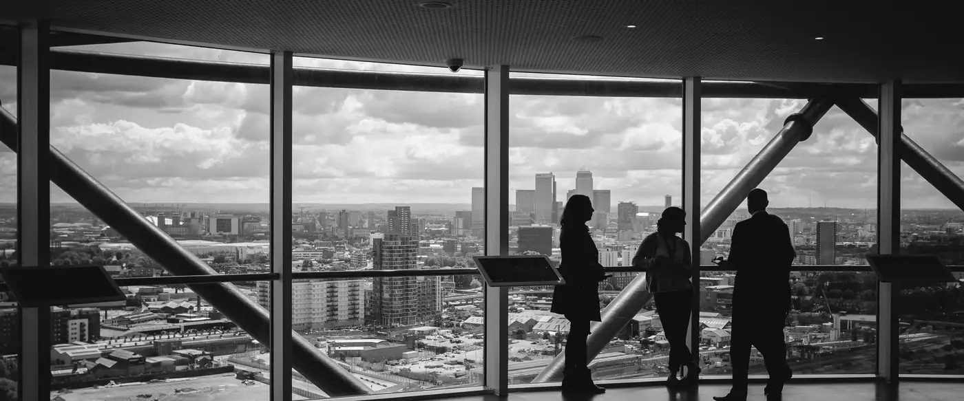 Three colleagues talking beside a floor-to-ceiling office window, with a city skyline behind them