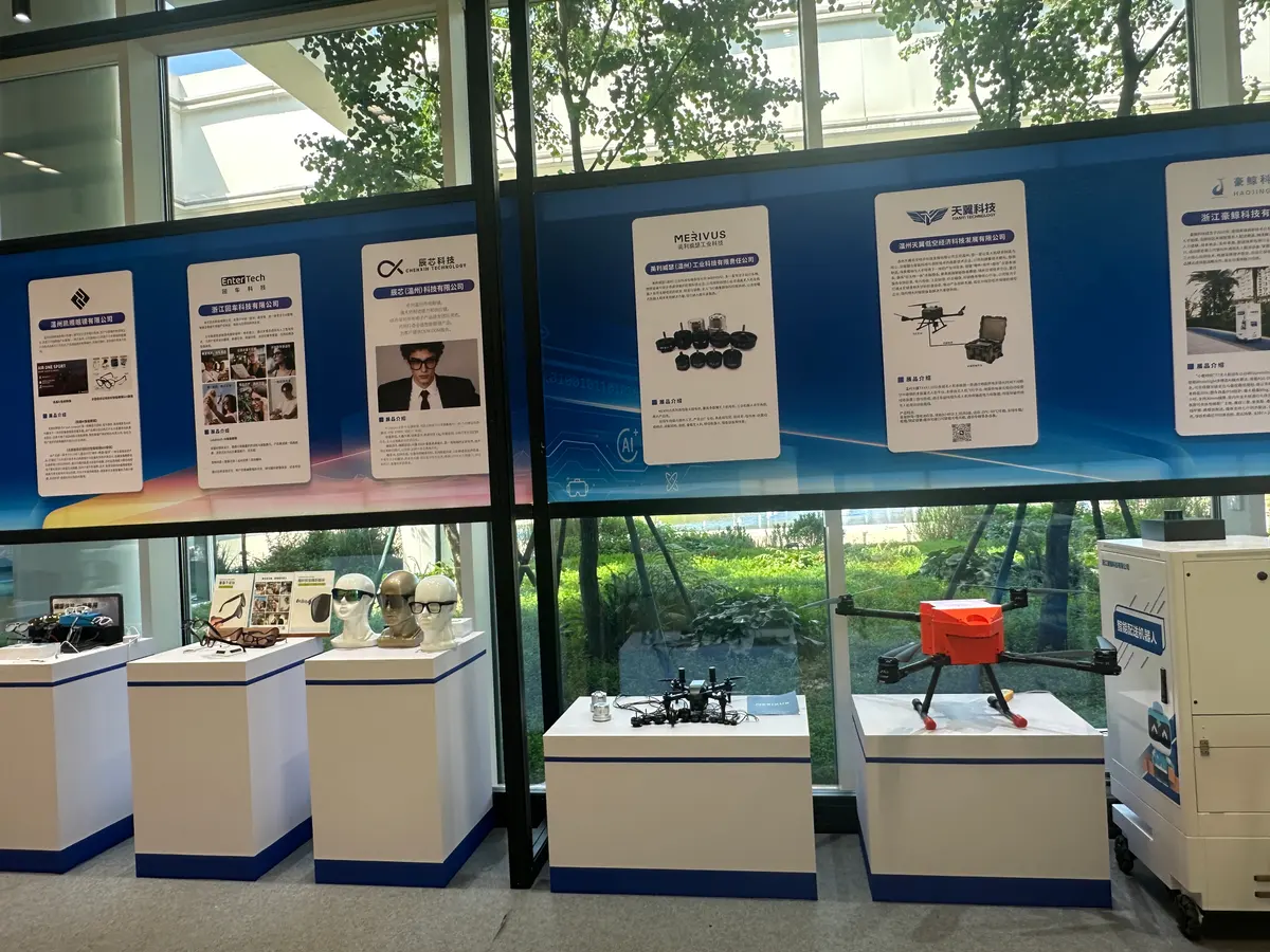 AI glasses on mannequin heads and display plinths beneath exhibitor panels for Wenzhou eyewear companies, with a drone on a plinth to the right