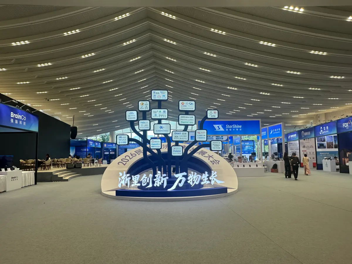 Exhibition hall with a tree-shaped installation carrying exhibitor logos above the title 浙里创新 万物生长, and exhibitor stands on both sides