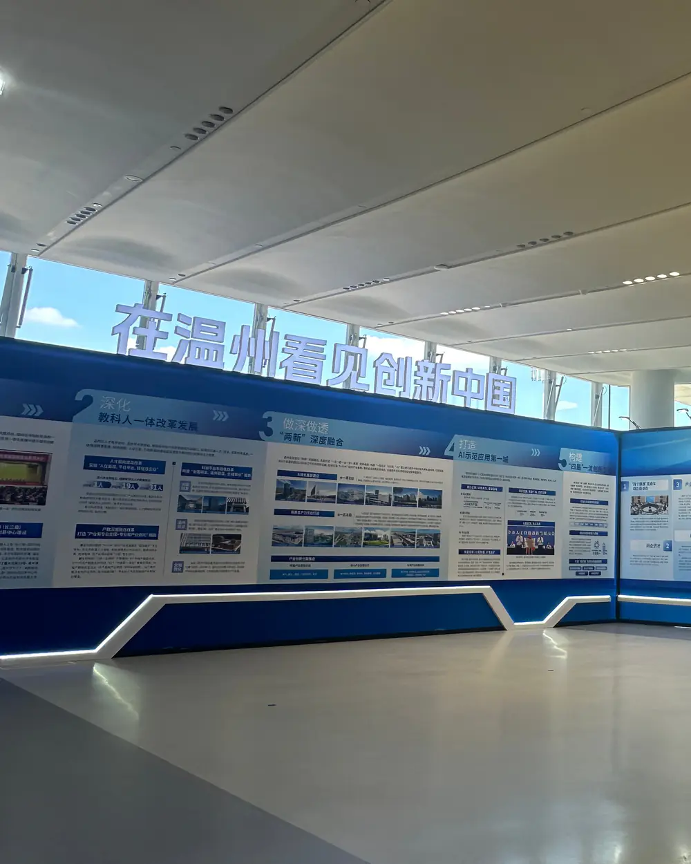 A long gallery of illuminated exhibition panels in the China Pavilion, under a white ceiling and tall windows