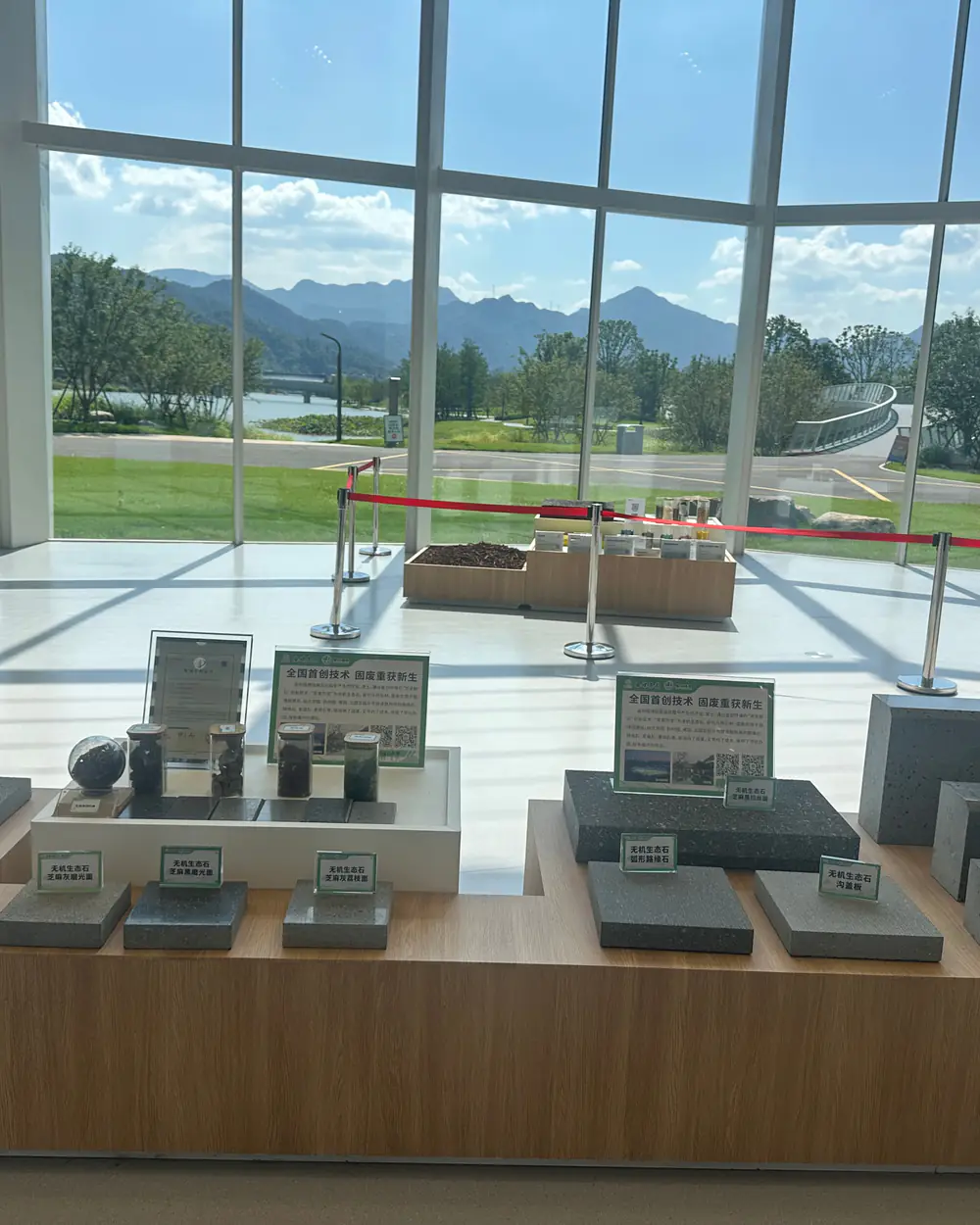 View through the glass wall of the China Pavilion to lawns, a river and mountains, with material samples on display in the foreground