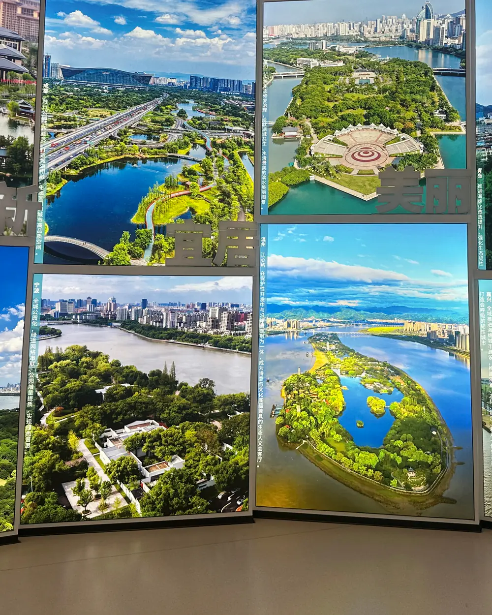 A wall of large illuminated aerial photographs of Wenzhou, showing parks, rivers, bridges and the city skyline